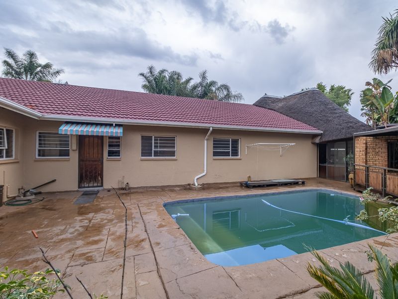 Rear exterior view of the farm property featuring a swimming pool, paved patio area, and a combination of tiled and thatched roofing.