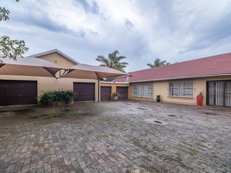 Spacious paved driveway area featuring multiple garage doors, a protective shade sail, and secure window bars on the main building facade.