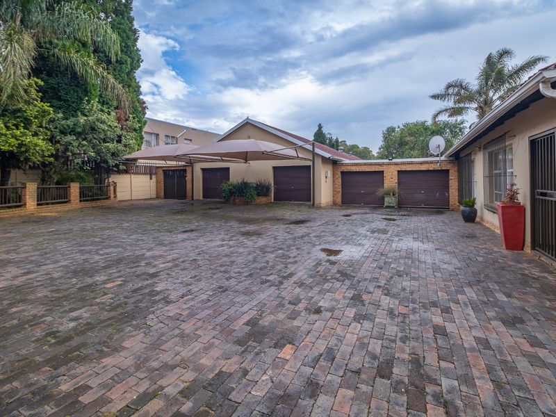 Spacious paved driveway area featuring a triple garage with roller doors and overhead shade sail protection, set within a secure walled property boundary.