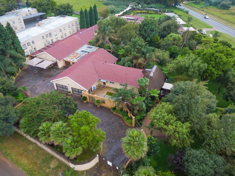 Aerial view of a farm property featuring a large main residence with a tiled roof, paved driveway, swimming pool, and extensive mature garden landscaping.