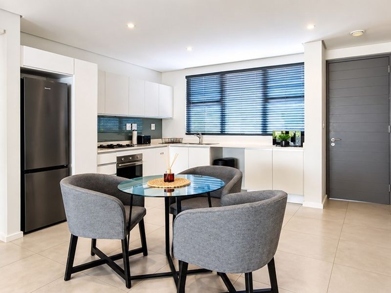 Modern open-plan kitchen featuring sleek white cabinetry, integrated appliances, tiled flooring, and recessed lighting, seamlessly flowing into the dining area.