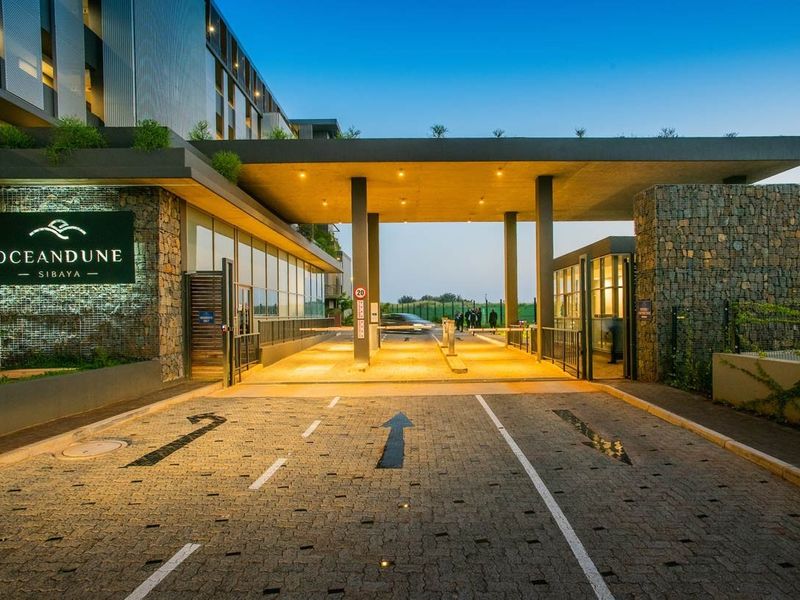 The secure entrance to the Oceandune Sibaya apartment complex, featuring modern stone cladding, a paved driveway, and professional lighting.