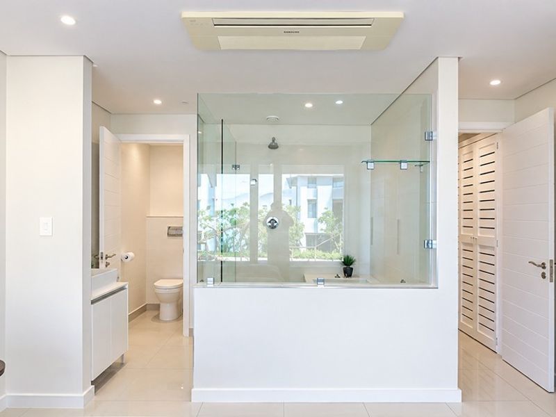 Modern, bright bathroom featuring a glass-enclosed shower, wall-mounted toilet, vanity unit, and integrated ceiling air conditioning system with clean, neutral finishes.