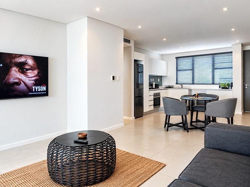 Modern open-plan living area featuring tiled floors, recessed lighting, and a sleek kitchen with built-in appliances and contemporary finishes.