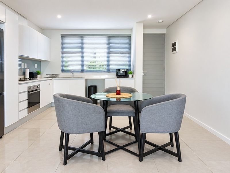 Modern open-plan kitchen and dining area featuring sleek white cabinetry, integrated appliances, tiled flooring, and neutral finishes throughout.