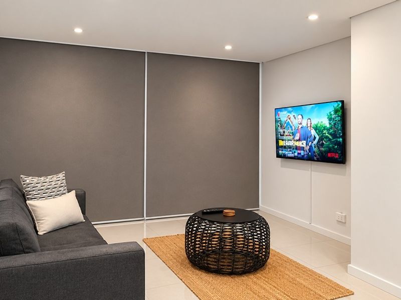 A modern, well-maintained living room featuring neutral tiled flooring, recessed downlighting, and a clean, minimalist aesthetic with built-in storage.