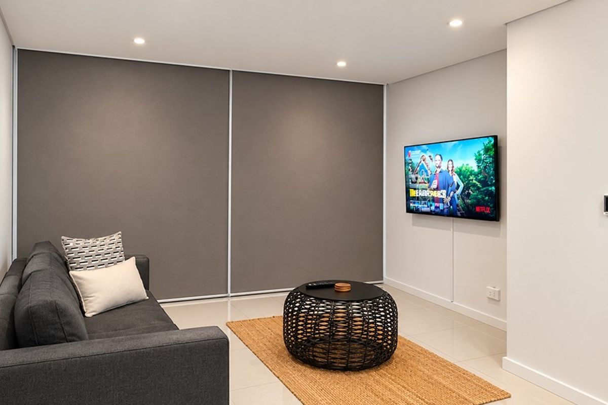 A modern, well-maintained living room featuring neutral tiled flooring, recessed downlighting, and a clean, minimalist aesthetic with built-in storage.