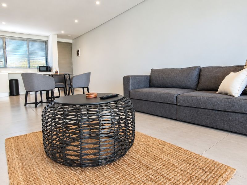 Modern open-plan living and dining area featuring neutral tiled flooring, recessed lighting, and a functional kitchen corner with clean cabinetry.