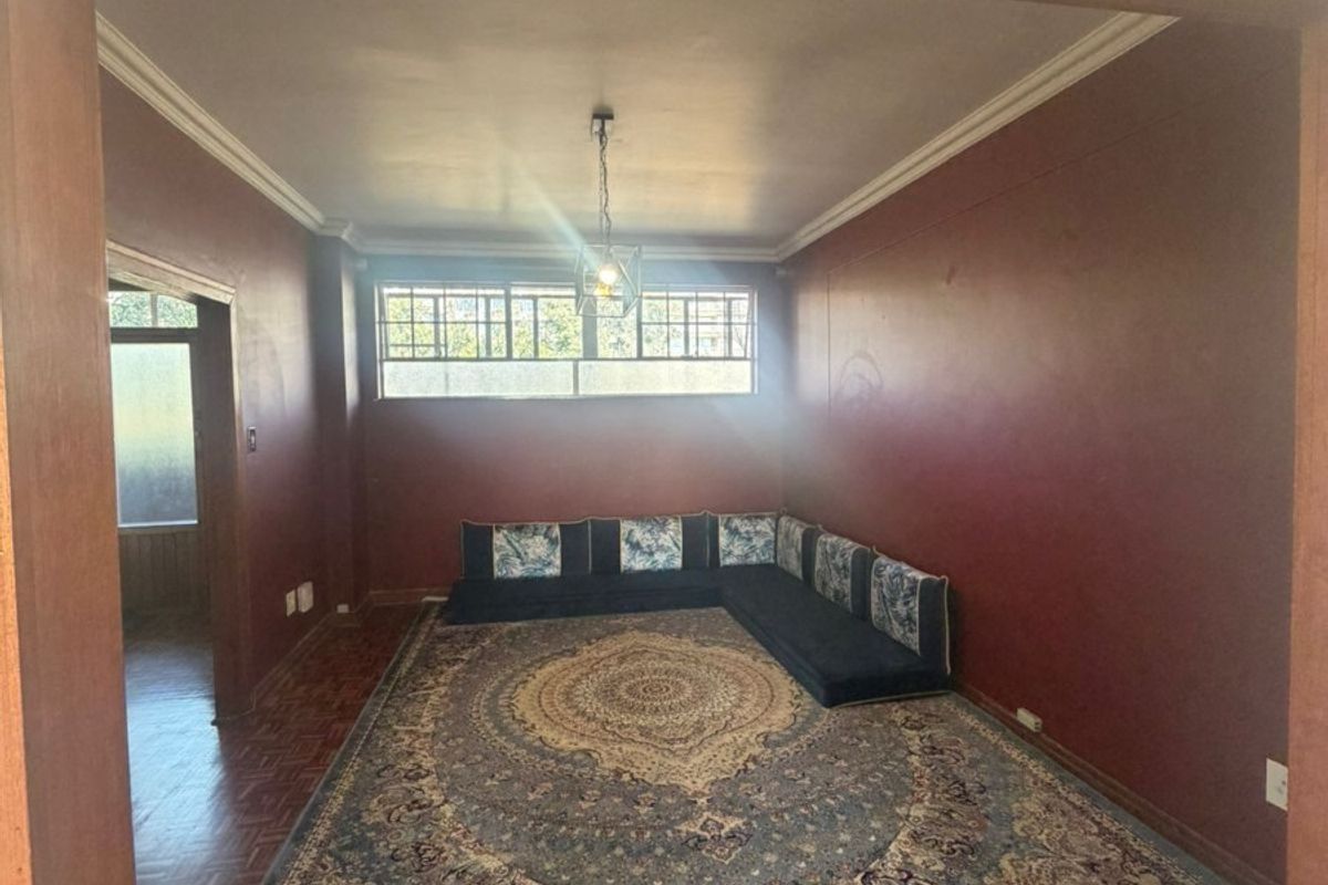 A living room featuring traditional parquet flooring, decorative ceiling cornicing, and a pendant light fixture, framed by a solid timber doorway.