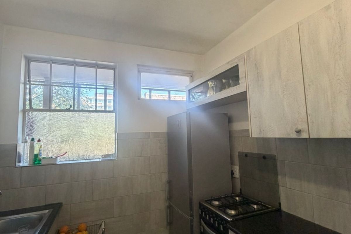 A functional kitchen featuring built-in cabinetry, a gas stove, stainless steel sink, and tiled finishes, offering a practical layout for daily meal preparation.