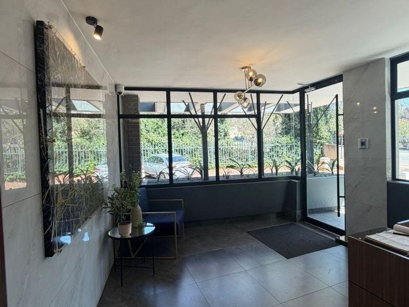 Modern apartment building entrance lobby featuring large format floor tiles, marble-look wall cladding, and floor-to-ceiling black framed glass windows.