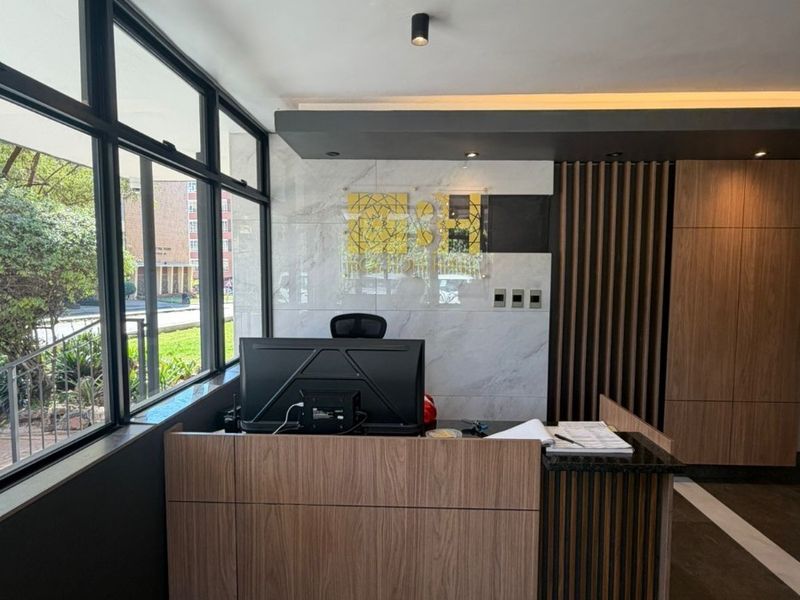 Modern apartment building reception area featuring a custom built-in desk, marble wall accents, timber paneling, and large windows providing natural light.