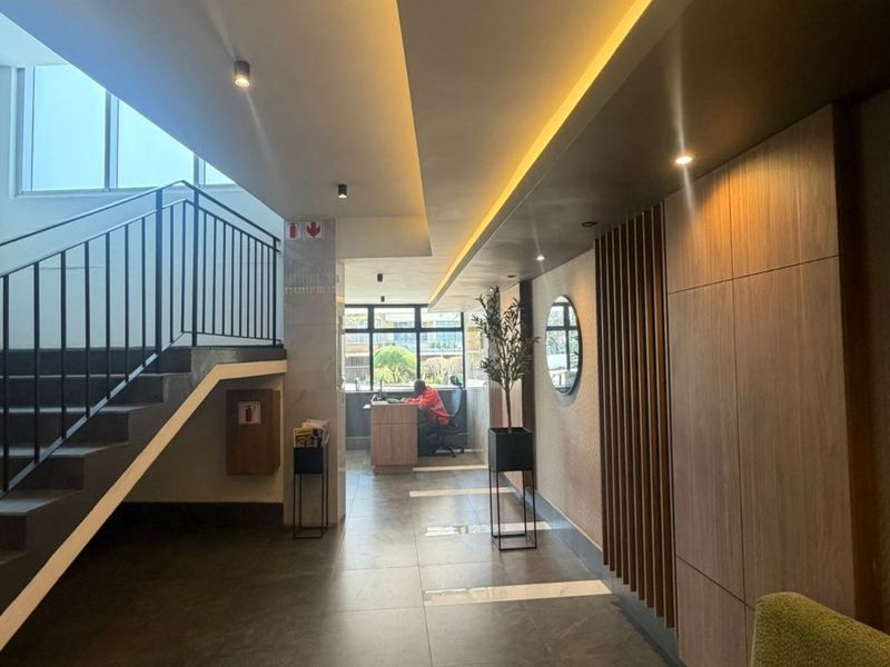Modern apartment building entrance lobby featuring sleek tiled floors, wood-paneled walls, recessed lighting, and a contemporary staircase with a metal balustrade.