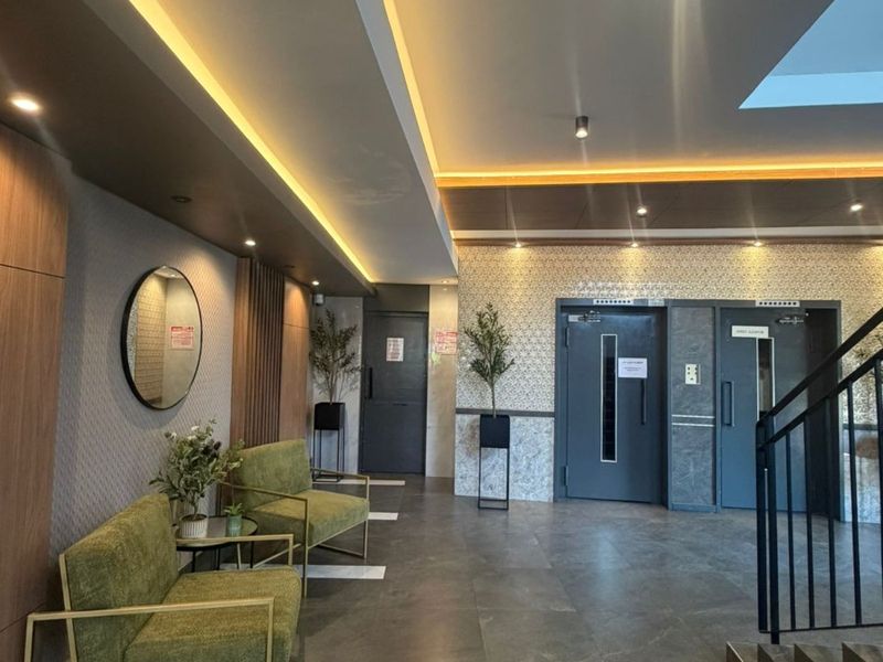 Modern apartment building lobby featuring tiled flooring, recessed cove lighting, elevator access, and a contemporary staircase.