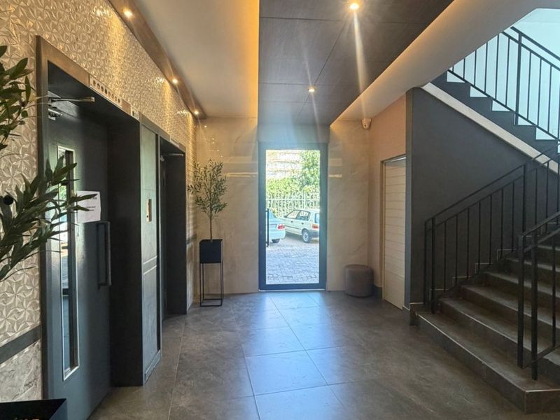 Modern apartment building entrance lobby featuring a sleek elevator, tiled flooring, and a contemporary staircase with metal railings.