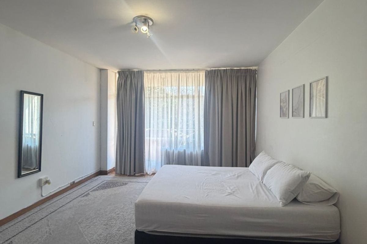 A spacious bedroom featuring parquet flooring, neutral walls, and large windows with floor-to-ceiling curtains, providing a bright and comfortable living space.