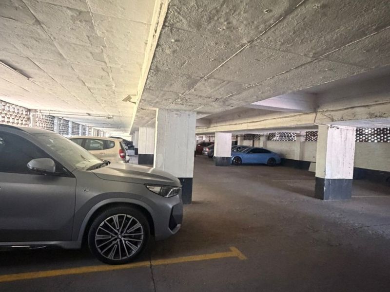 Undercover parking garage area featuring concrete structural columns and ceiling with ventilation blocks along the perimeter.