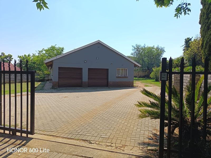 Front view of a property featuring a double garage, paved driveway, and secure gated entrance with established garden surroundings.