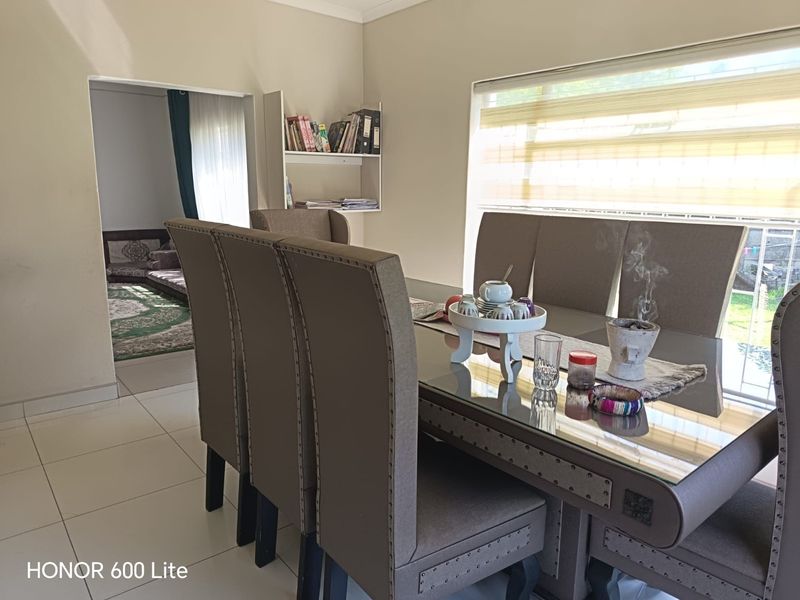 A dining room featuring tiled flooring, built-in wall shelving, and large windows with roller blinds, providing a functional space for meals.