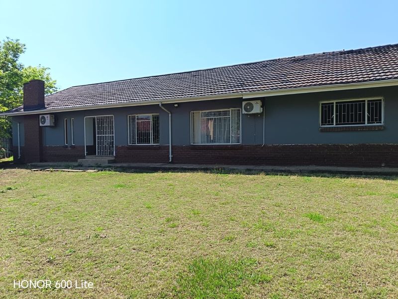 Rear view of the house featuring a tiled roof, brick chimney, security bars on windows, and an installed air conditioning unit.