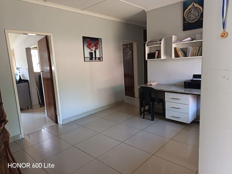 A living area featuring neutral tiled flooring, a built-in desk with storage drawers, and wall-mounted shelving units.