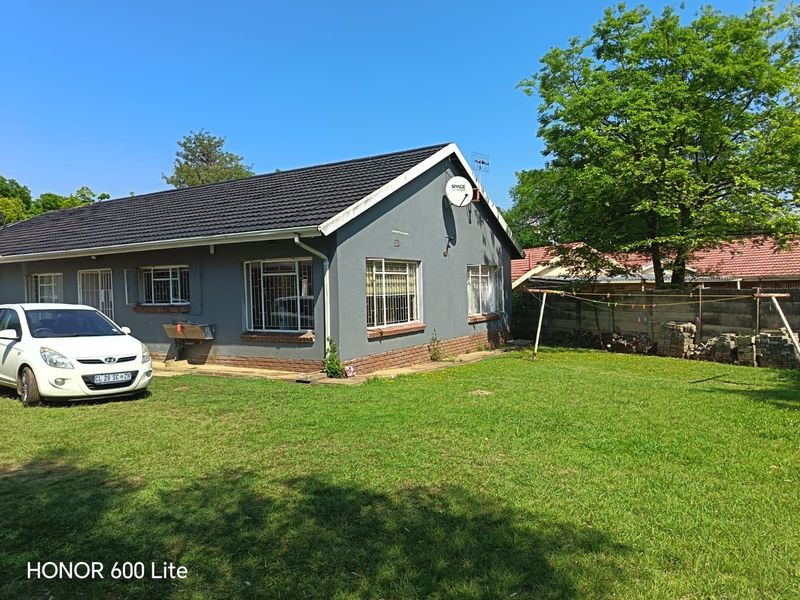 Rear view of a single-story house featuring a tiled roof, security bars on windows, and a spacious lawn area.