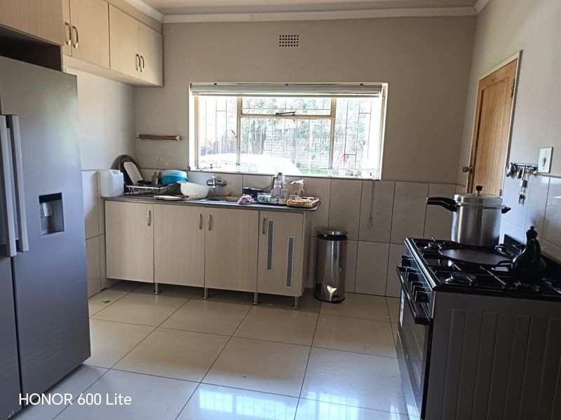Functional kitchen featuring light-toned built-in cabinetry, tiled flooring, a stainless steel sink, and a freestanding gas stove with a tiled backsplash.