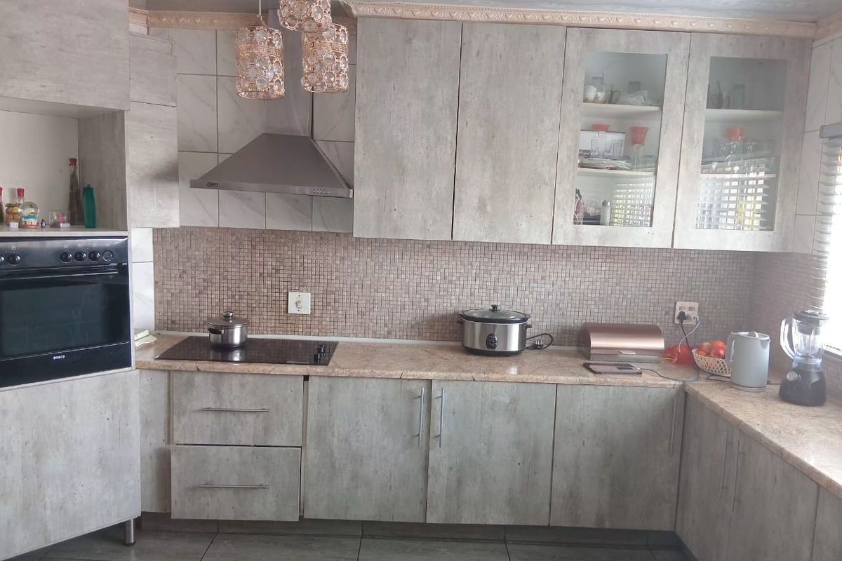 A functional kitchen featuring modern grey laminate cabinetry, stone countertops, a mosaic tile backsplash, and integrated appliances including an oven and extractor fan.