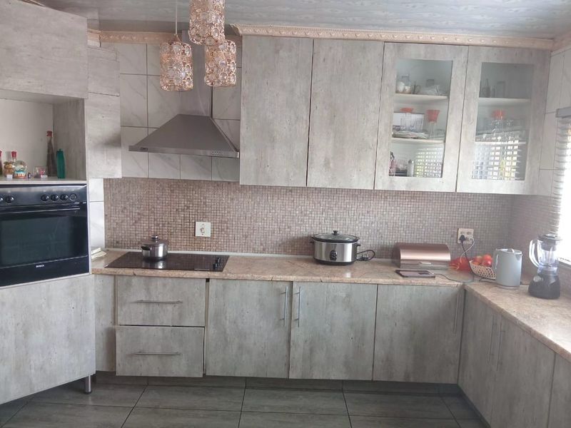 A functional kitchen featuring modern grey laminate cabinetry, stone countertops, a mosaic tile backsplash, and integrated appliances including an oven and extractor fan.