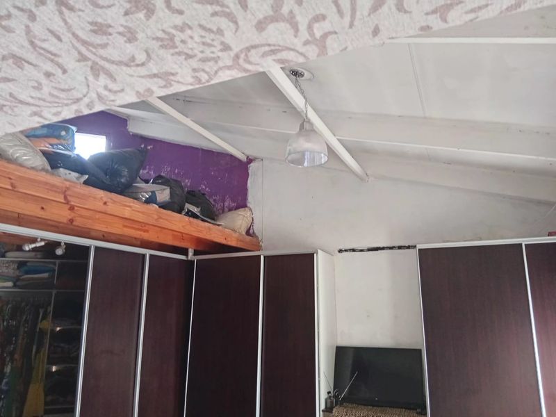 Bedroom featuring built-in cupboards, exposed rafters, and a mezzanine storage area, requiring cosmetic updates to improve the overall finish and aesthetic appeal.