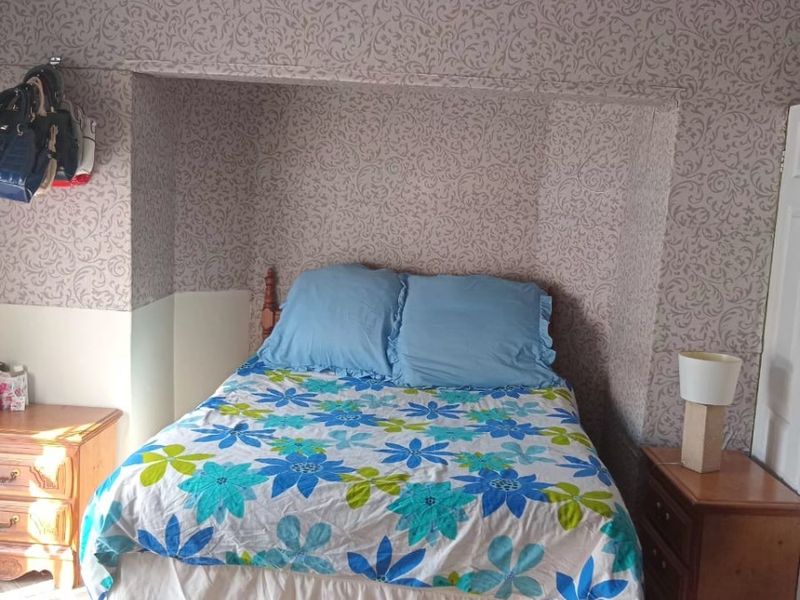 A bedroom featuring tiled flooring and a recessed alcove area with patterned wallpaper.