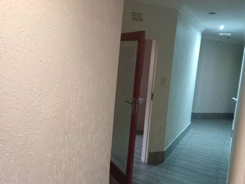 A functional hallway featuring tiled flooring, textured walls, and recessed downlighting, providing access to adjacent rooms.