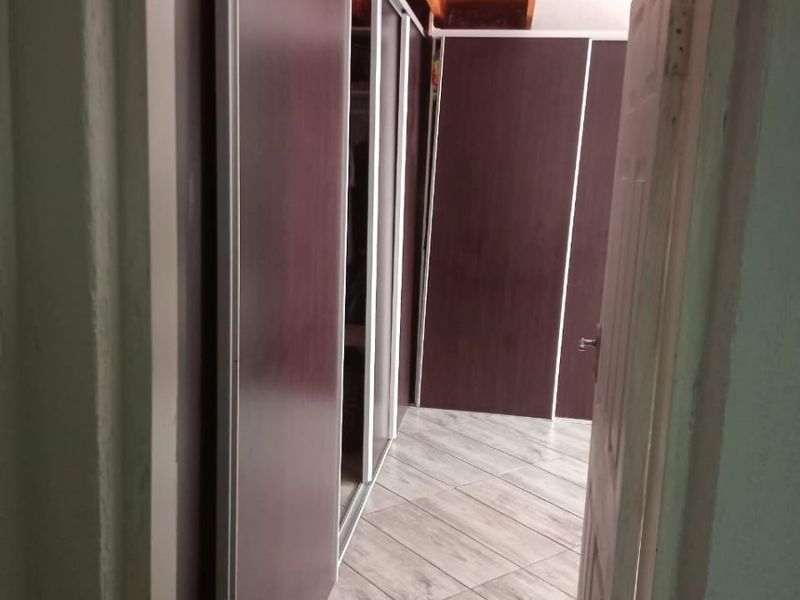 A bedroom interior featuring built-in cupboards, tiled flooring, and exposed timber ceiling beams, viewed through a doorway.