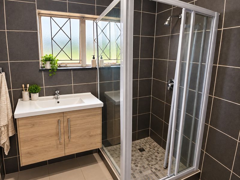 Modern bathroom featuring a floating wood-finish vanity, basin, and a glass-enclosed shower with dark charcoal wall tiling and mosaic floor accents.