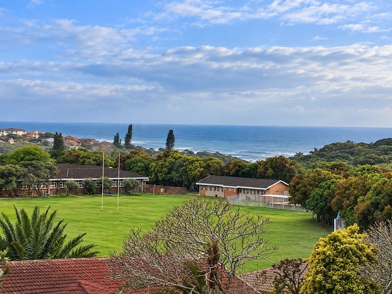 A scenic elevated view overlooking a green field, surrounding coastal vegetation, and the ocean in the distance.
