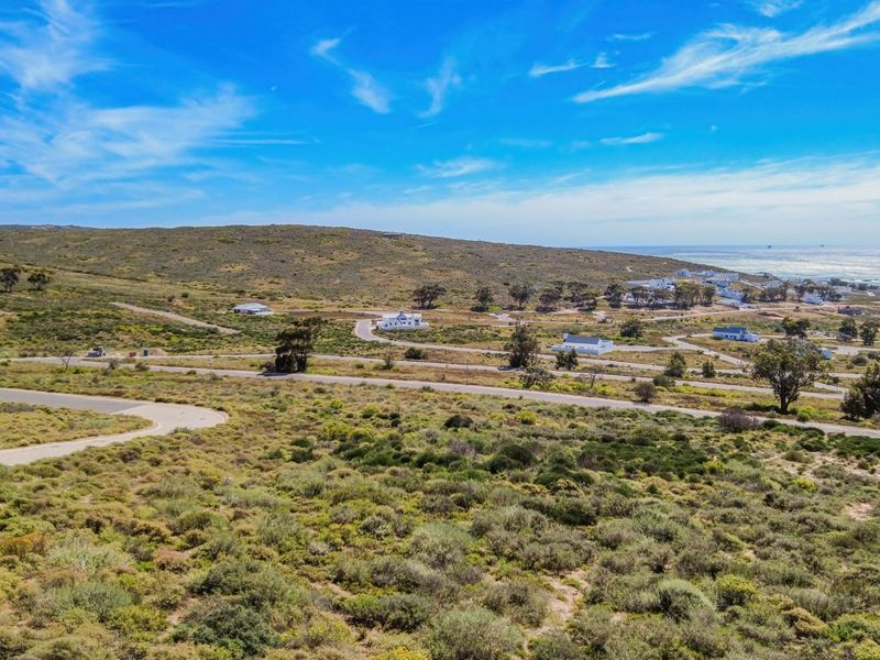 An aerial view of a coastal residential estate featuring paved roads and natural vegetation with ocean views in the distance.