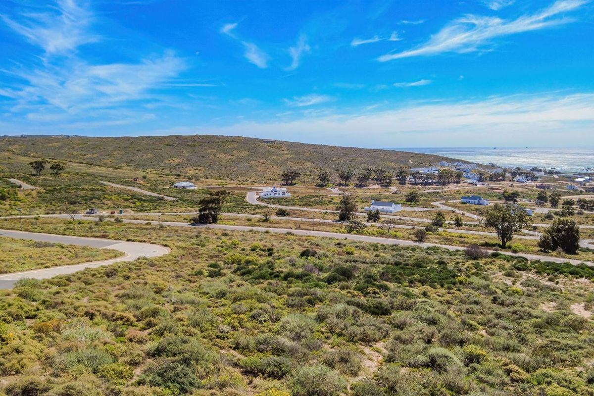 An aerial view of a coastal residential estate featuring paved roads and natural vegetation with ocean views in the distance.