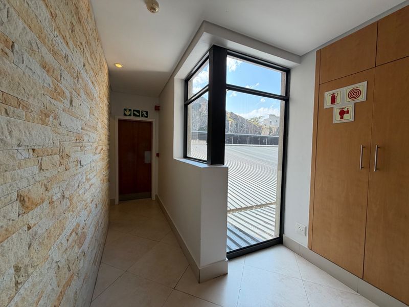 A clean, modern office hallway featuring a textured stone feature wall, built-in storage cabinetry, and a corner window providing natural light.