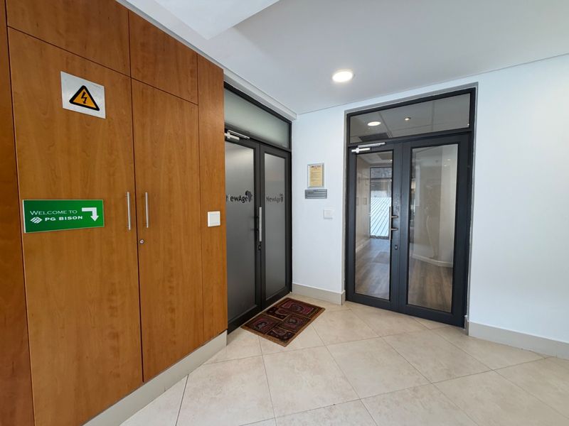 A clean and professional office entrance featuring modern glass-panelled doors, built-in wooden cabinetry, and neutral tiled flooring.
