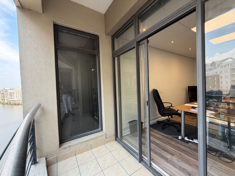 A covered balcony area featuring tiled flooring and a sliding glass door providing access to an office space with a view.