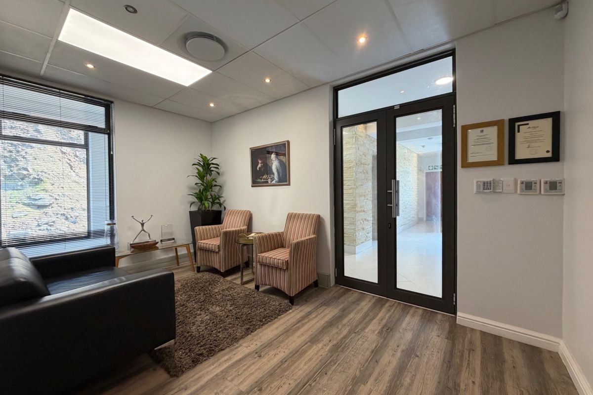 A professional office reception area featuring modern laminate flooring, a suspended ceiling with recessed lighting, and a secure double glass entrance door.
