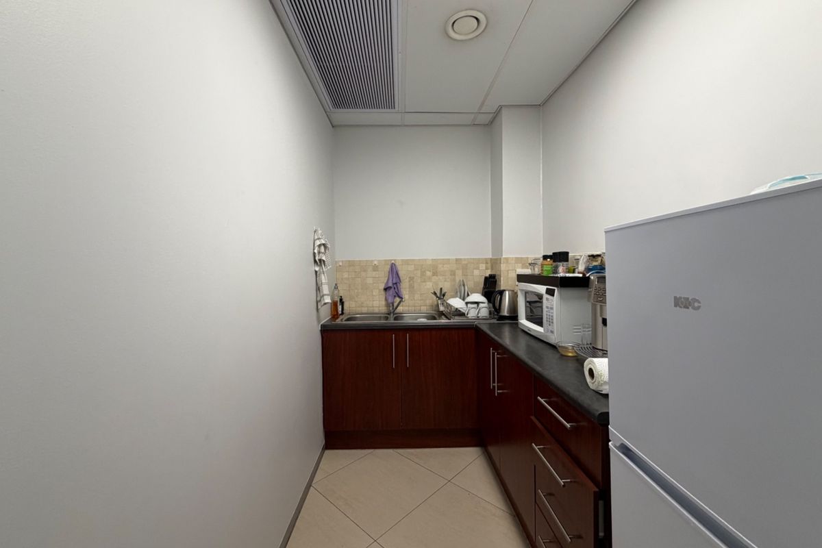A compact office kitchenette featuring dark wood cabinetry, a double bowl sink, tiled backsplash, and integrated air conditioning.