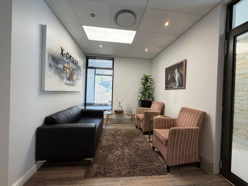 A professional office waiting area featuring laminate flooring, recessed ceiling lighting, and a glass entrance door.