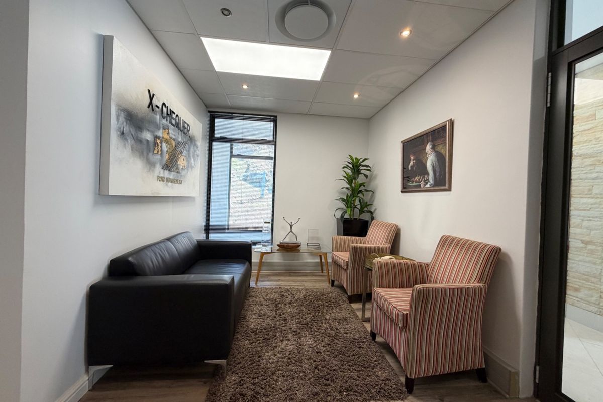 A professional office waiting area featuring laminate flooring, recessed ceiling lighting, and a glass entrance door.