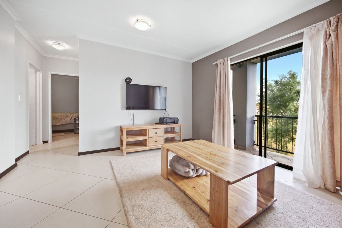 Bright living room featuring tiled flooring, neutral walls, and a sliding glass door providing access to a private balcony.
