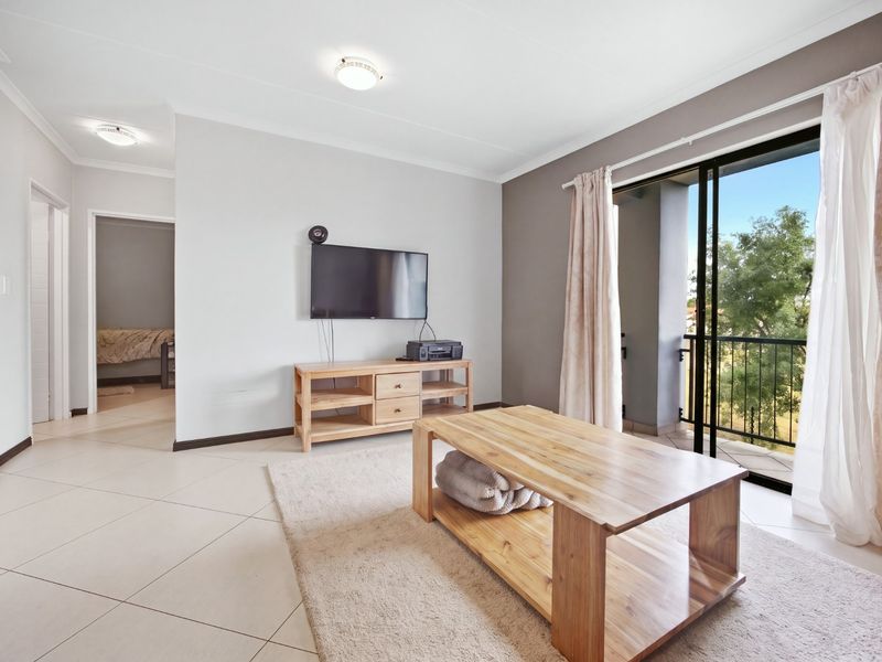Bright living room featuring tiled flooring, neutral walls, and a sliding glass door providing access to a private balcony.