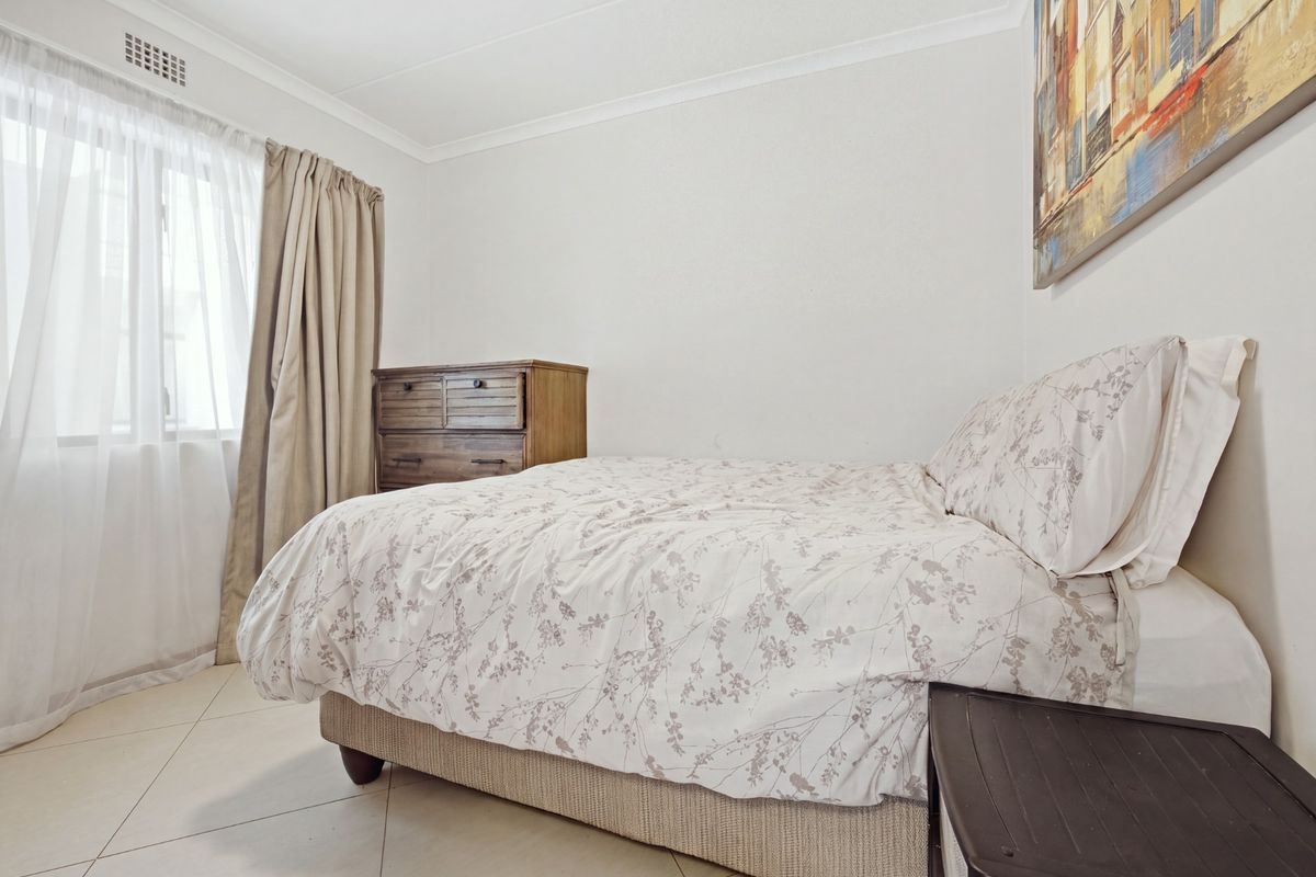 A functional bedroom featuring tiled flooring, neutral walls, and a window with curtain treatments.