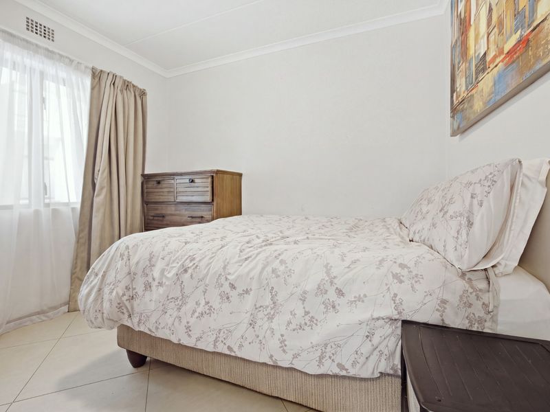 A functional bedroom featuring tiled flooring, neutral walls, and a window with curtain treatments.