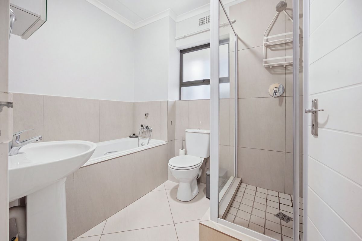 A clean, modern bathroom featuring a pedestal basin, a built-in bathtub, and a separate glass-enclosed shower with neutral wall and floor tiling.