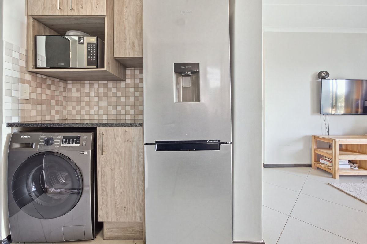 A modern kitchen area featuring light wood-toned cabinetry, a tiled backsplash, and integrated laundry appliances, seamlessly flowing into the adjacent living space.